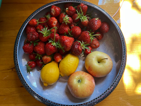 Close up bowl of strawberries, lemons apples, ripe juicy fruit berry harvest fresh organic country garden allotment orchard Summer in antique ceramic bowl wood kitchen backgroundの写真素材