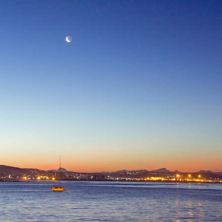 Sunset over the sea with a sailboat and a crescent moonの写真素材
