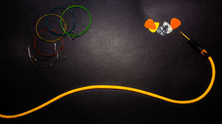 new multicolor guitar strings for acoustic guitar, ready for installation, guitar picks and an orange jack cable on dark gray backgroundの写真素材