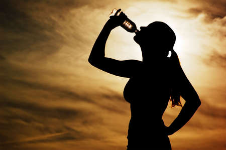 Beautiful young sporty woman drinking in front of a sunset.の写真素材