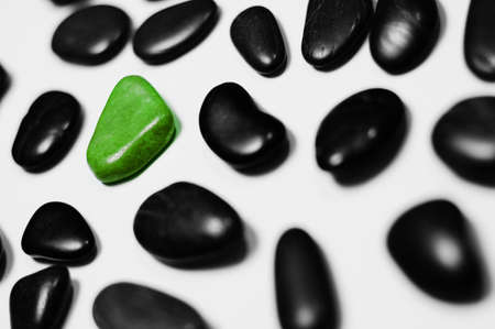 Green rock amid black rocks on a white background.の写真素材