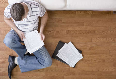 Young man sits on the floor as he looks through paperwork. Horizontal shot.の写真素材