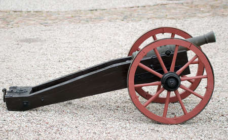 There is old cannon, black, red, road of stone