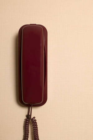 Red telephone is hanging on light brown wallの写真素材