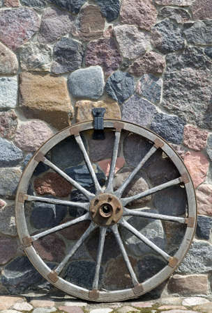 Old wooden wheel is placed near wall made from stoneの写真素材