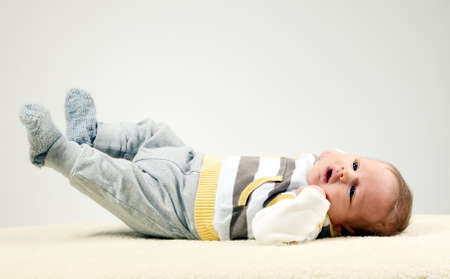 Beautiful white baby boy with big eyes is lying on furry blanketの写真素材