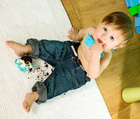 Child with blue bow-tie is celebrating his first birthday and eats cake