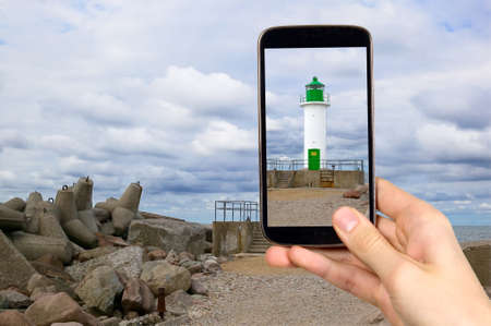Man is taking photo of green lighthouse with smart mobile phoneの写真素材