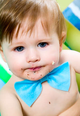 Child with blue bow-tie is celebrating his first birthday and eats cakeの写真素材