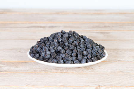 Dried black aronia berries in plate on wooden backgroundの写真素材