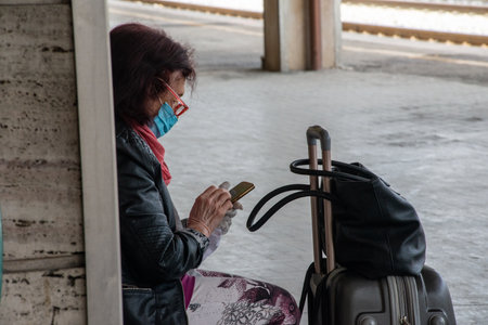 terni,italy may 29 2020:woman waiting for train to leave holding smartphone and has mask for covid emergencyのeditorial素材