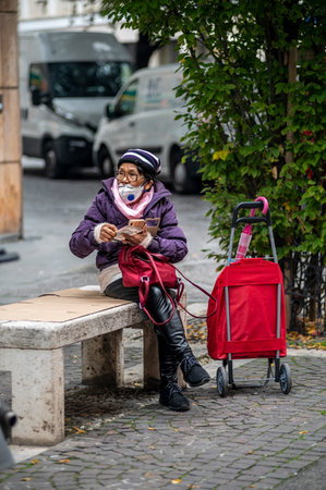 terni, itali november 05 2020: elderly oriental woman with medical mask sitting on a bench on the phoneのeditorial素材