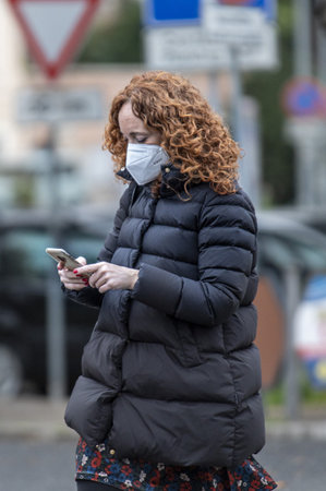 terni, italy jenuary 22 2021: man wearing medical mask sitting on a bench and looking at cellphoneのeditorial素材