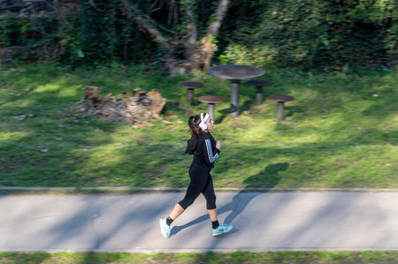 terni, italy february 20 2021: panning of woman running in park with headphonesのeditorial素材
