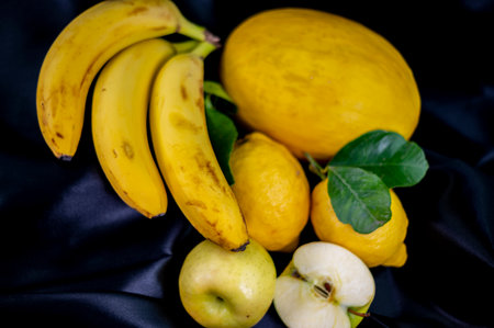 yellow fruit on a black background with melon bananas apples and lemonsの写真素材