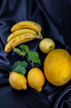 yellow fruit on a black background with melon bananas apples and lemonsの写真素材