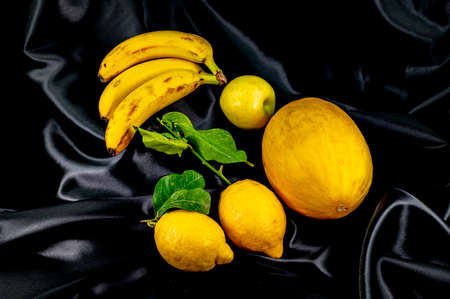yellow fruit on a black background with melon bananas apples and lemonsの写真素材