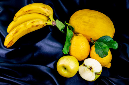 yellow fruit on a black background with melon bananas apples and lemonsの写真素材
