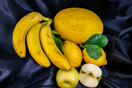yellow fruit on a black background with melon bananas apples and lemonsの写真素材