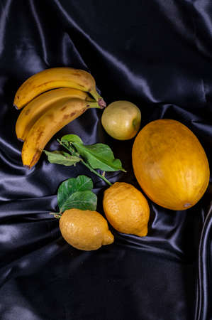 yellow fruit on a black background with melon bananas apples and lemonsの写真素材