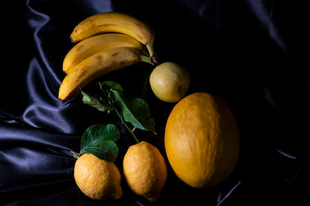 yellow fruit on a black background with melon bananas apples and lemonsの写真素材