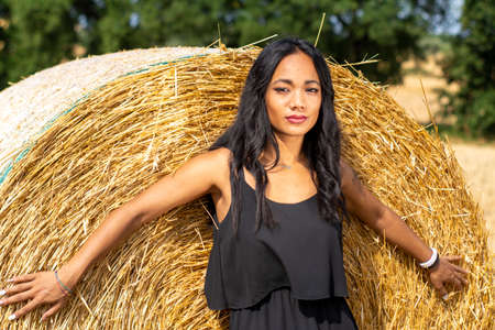 Indian girl leaning against a hay bale on a sunny dayの写真素材