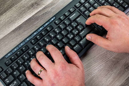 hands of a man typing on the keyboard pcsu wooden tableの写真素材