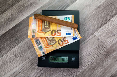 euro banknotes on top of a scale with cigar on a wooden tableの写真素材