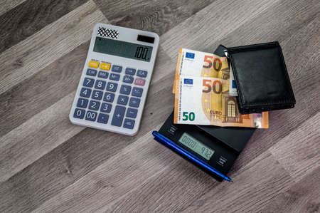 euro banknotes on top of a scale with calculator nearby on a wooden tableの写真素材
