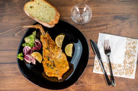 monkfish au gratin plate with composition on wooden top and wine glass and cutleryの写真素材