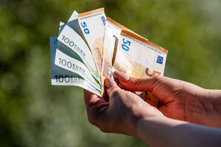banknotes of 50 and 100 euros in the hands of a woman background in natureの写真素材