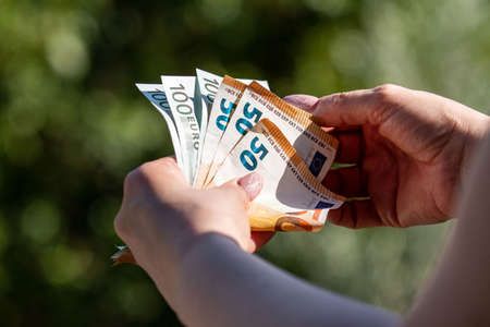 banknotes of 50 and 100 euros in the hands of a woman background in natureの写真素材