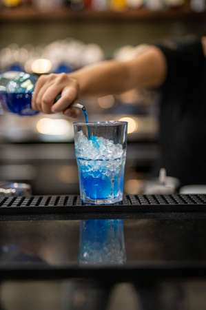 woman's hand pouring blue liqueur into a glass with iceの写真素材