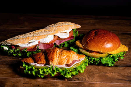 composition of sandwiches with salami and vegetables on a wooden surfaceの写真素材