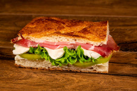 sandwich with salami and vegetables on a wooden surfaceの写真素材