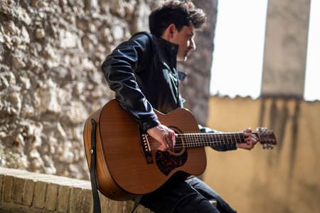 boy plays guitar outdoors in an alley of a village in the daytimeの写真素材
