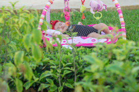 Beautiful baby girl sleeping in her garden, on grass on colorful rugの写真素材