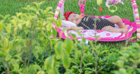 Beautiful baby girl sleeping in her garden, on grass on colorful rugの写真素材