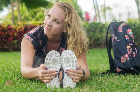 Blonde girl, does exercise sitting on the grass, stretches her body facing camera, towards her feet...