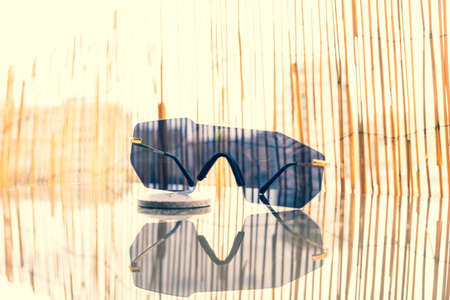 Futuristic sunglasses rimless design with black lens on a table with bamboo fence background. Selective Focusの写真素材