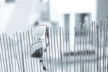 Classic model Sunglasses with metal frame and black lense hanging on bamboo fence. Selective focus