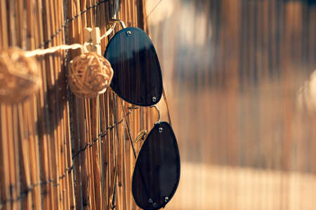 Aviator Sunglasses model with big black lenses for men hanging on a bamboo fence in a sunny day. Selective focusの写真素材