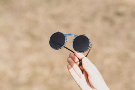 Steampunk sunglasses held in hand with round lenses retro flip up model close up shoot in a summer day. Selective focusの写真素材