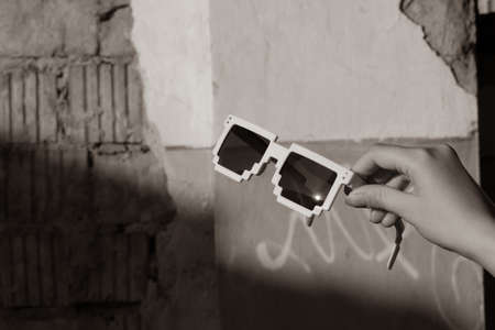 White pixel sunglasses with black lenses hold in hand closeup in a sunny day. Selective focusの写真素材