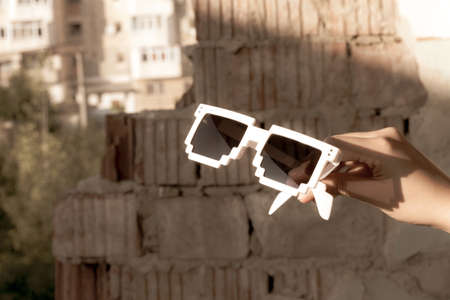 White pixel sunglasses with black lenses hold in hand closeup in a sunny day. Selective focus