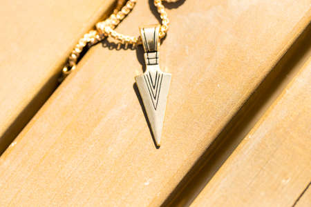 Pendant arrow necklace golden color shoot in a sunny day outside closeup. Selective Focusの写真素材