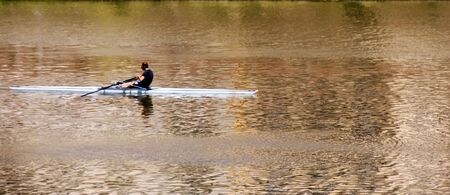 Man rowing down golden reflecting riverの写真素材