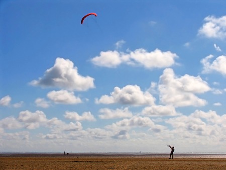 Lonesome figure flying kite over barren landscape, on beautiful day with blue sky and white cloudsの写真素材
