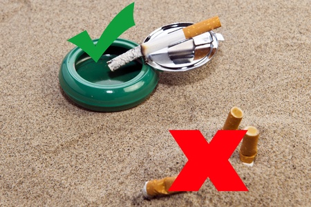 Cigarette in a small ashtray and cigarette butts in the sand