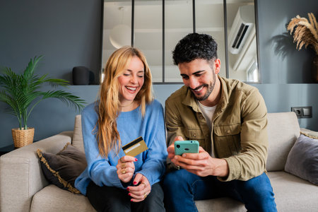 Young couple sittiong on the sofa shopping in e-commerce app with the smartphone and paying with a...